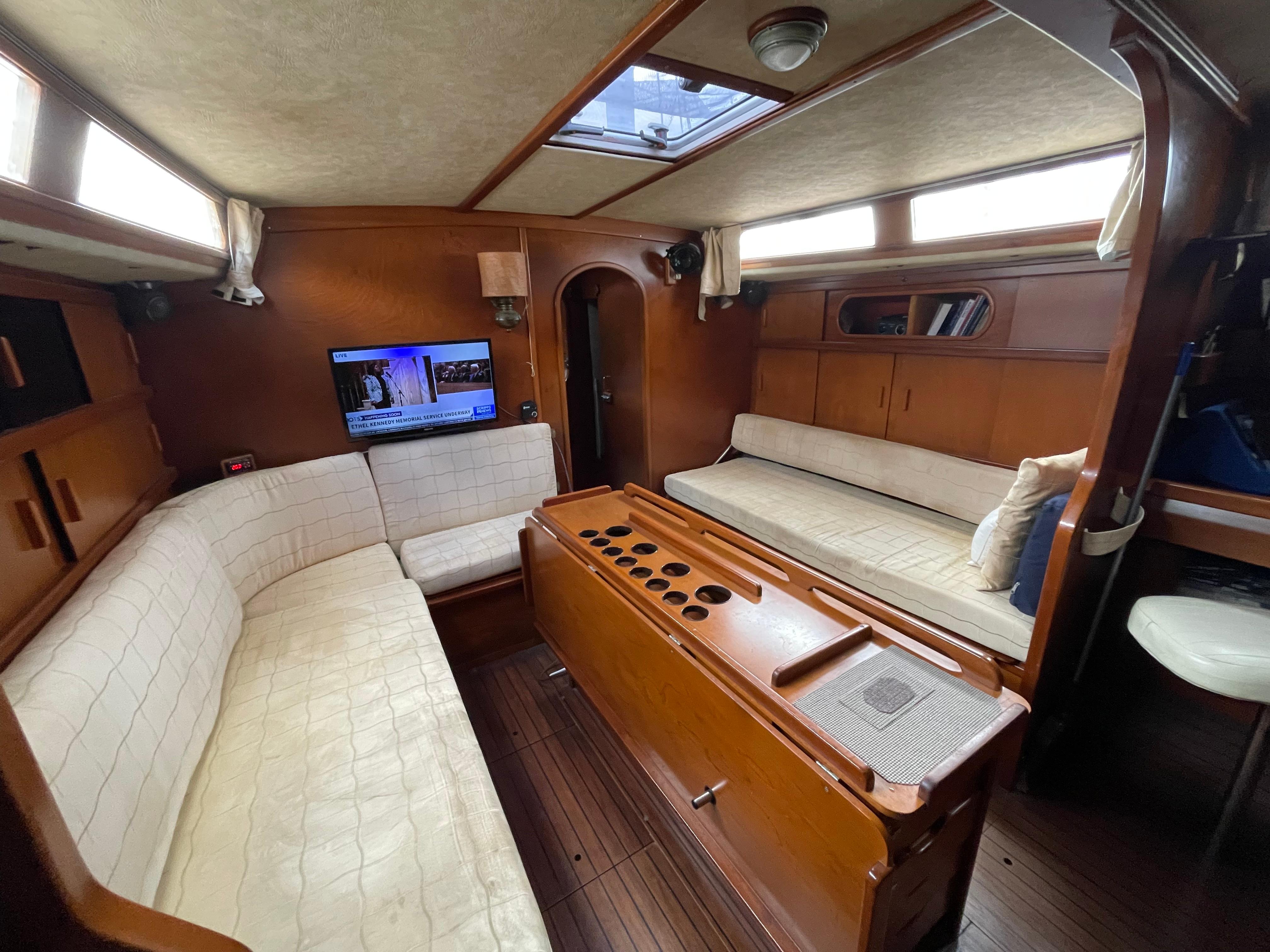 1985 Amel Maramu yacht interior with cozy seating, wooden finishes, and a mounted TV.