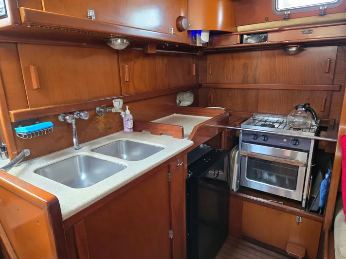 Bearaway Yacht Photos Pics 1985 Amel Maramu yacht kitchen with dual sinks, stove, and wooden cabinetry.
