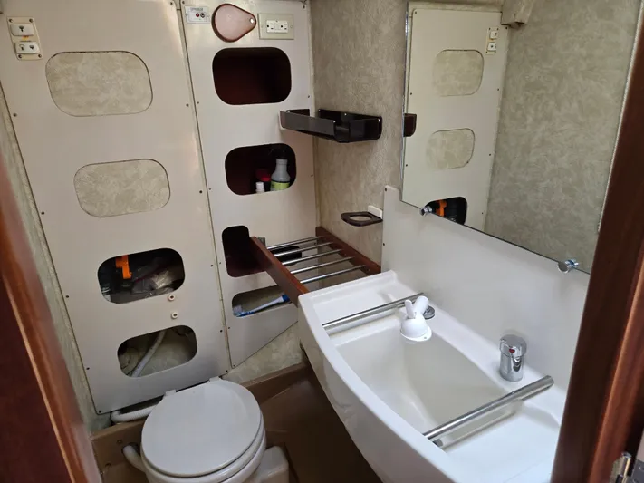 Bearaway Yacht Photos Pics Compact bathroom in a 1985 Amel Maramu sailboat, featuring a sink, toilet, and storage shelves.