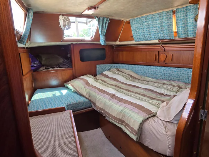Bearaway Yacht Photos Pics Cozy cabin interior of 1985 Amel Maramu sailboat with striped bedding and wooden furnishings.