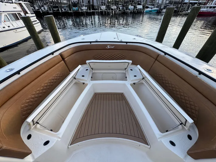  Yacht Photos Pics 2021 Scout 330 LXF boat interior with tan seating and storage compartments at a marina.