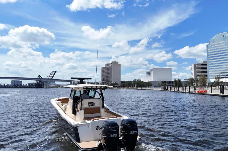  Yacht Photos Pics 2021 Scout 330 LXF boat cruising on a river with city skyline and bridge.