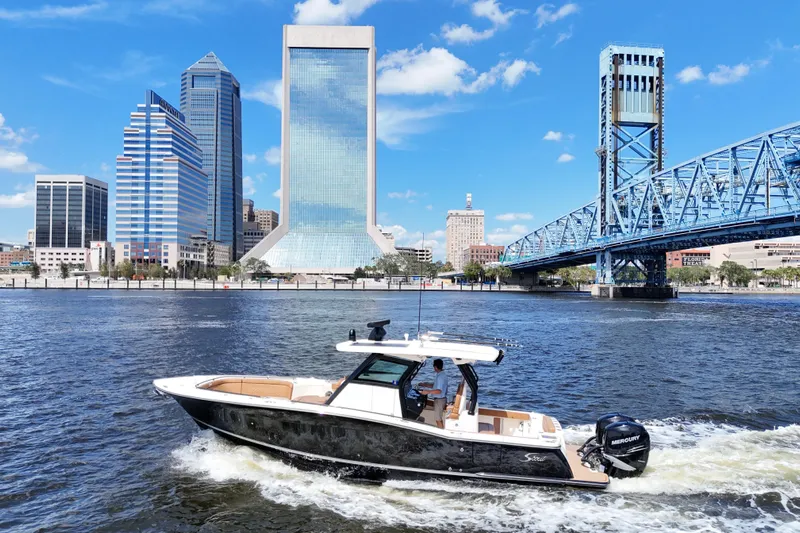  Yacht Photos Pics 2021 Scout 330 LXF boat cruising near city skyline and blue bridge on a sunny day.