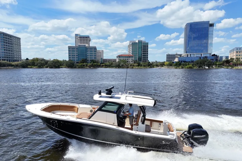  Yacht Photos Pics 2021 Scout 330 LXF boat cruising on a river with city skyline backdrop.