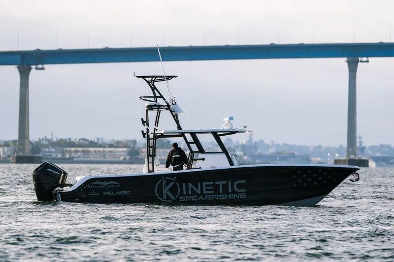 Reaper Yacht Photos Pics 2024 Invincible 33 Catamaran on water, featuring "Kinetic Spearfishing" branding, with bridge in background.
