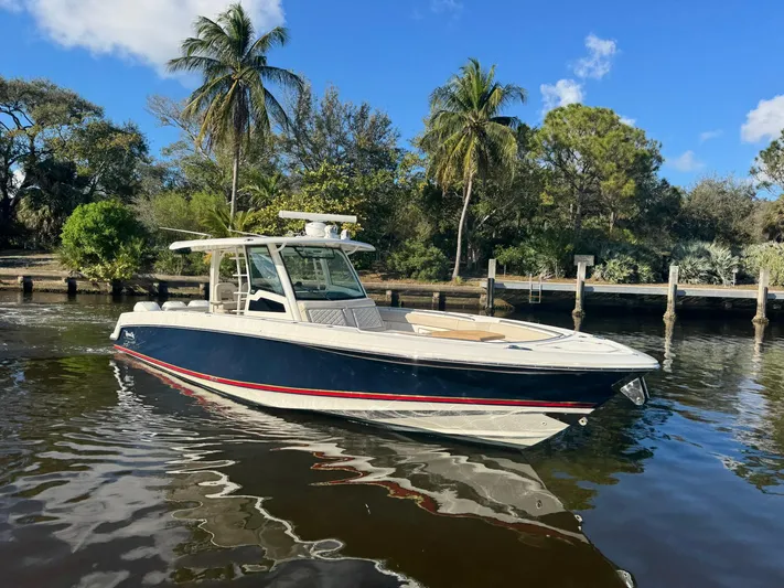  Yacht Photos Pics 2019 Boston Whaler 380 Outrage boat on calm water, surrounded by trees and blue sky.