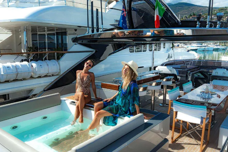 Clarity Yacht Photos Pics Women relaxing on a luxurious 2022 Riva 90' Argo yacht with a jacuzzi and dining area.