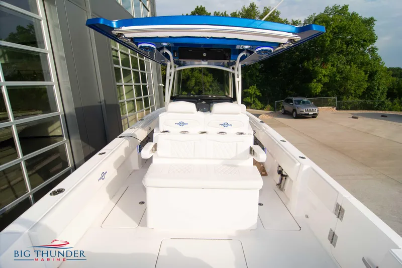  Yacht Photos Pics 2023 Fountain 34 CC boat with blue canopy, docked near a modern building.