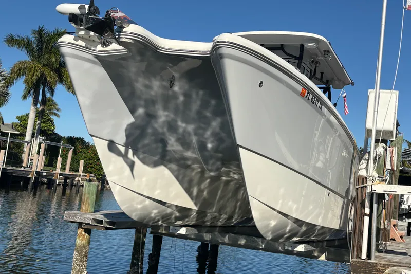  Yacht Photos Pics 2023 World Cat 295 CC boat on lift, reflecting sunlight, with palm trees in background.