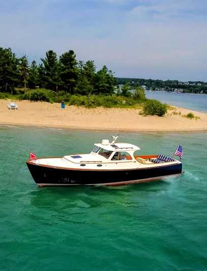 Luna Yacht Photos Pics Hinckley Picnic Boat 2000 cruising near a sandy beach with lush greenery.