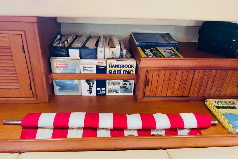 Resolute Yacht Photos Pics Nautical bookshelf on 2002 Island Packet 420 yacht with sailing guides and folded flag.