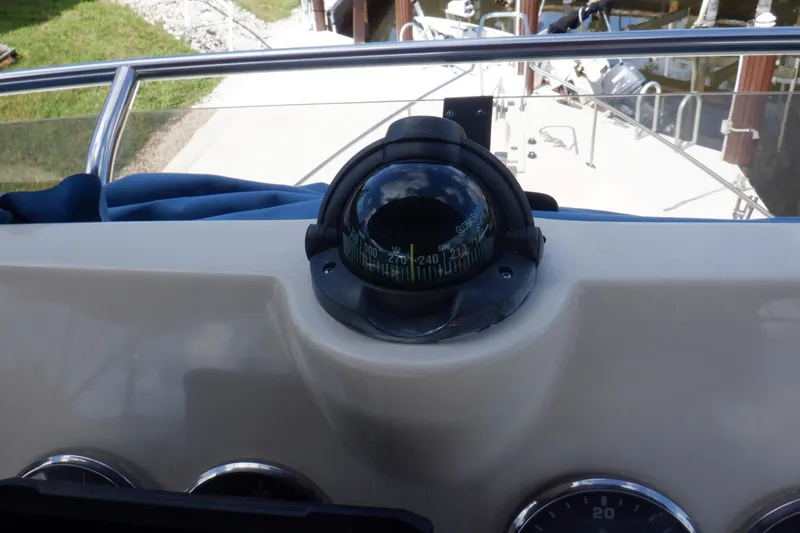 Betty Sue Yacht Photos Pics Compass on 2006 Mainship 34 Trawler dashboard, reflecting sky and surroundings.