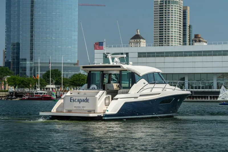 Escapade Yacht Photos Pics 2017 Tiara Yachts C44 Coupe cruising near city skyline, displaying "Escapade" on the stern.