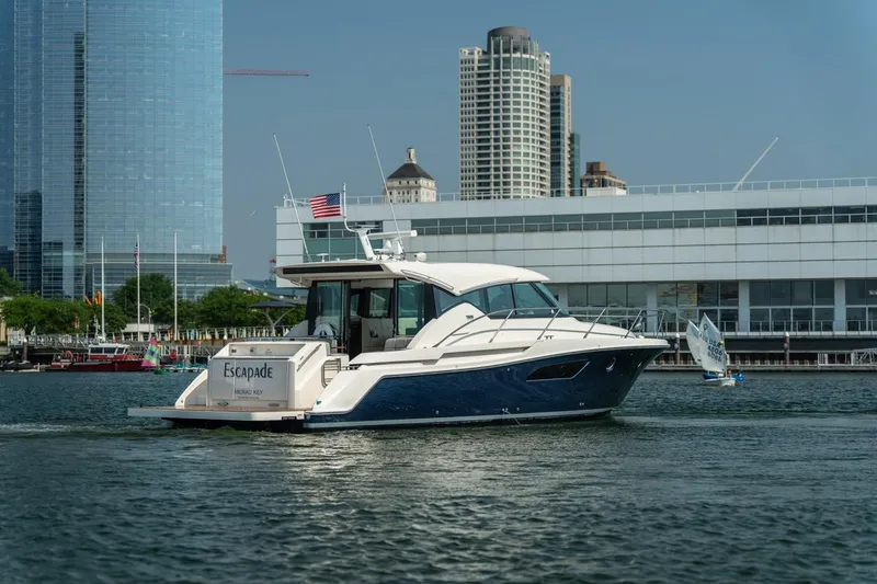 Escapade Yacht Photos Pics 2017 Tiara Yachts C44 Coupe cruising near city waterfront with modern buildings.