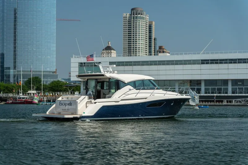 Escapade Yacht Photos Pics 2017 Tiara Yachts C44 Coupe cruising near urban waterfront buildings.