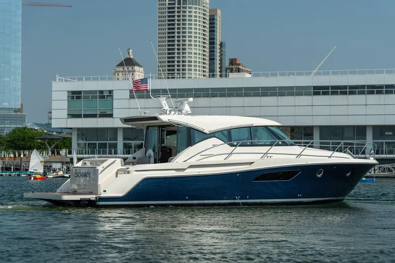 Escapade Yacht Photos Pics 2017 Tiara Yachts C44 Coupe cruising near modern waterfront buildings.