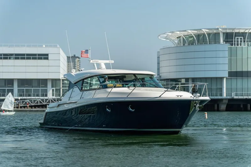 Escapade Yacht Photos Pics 2017 Tiara Yachts C44 Coupe cruising near modern waterfront buildings.