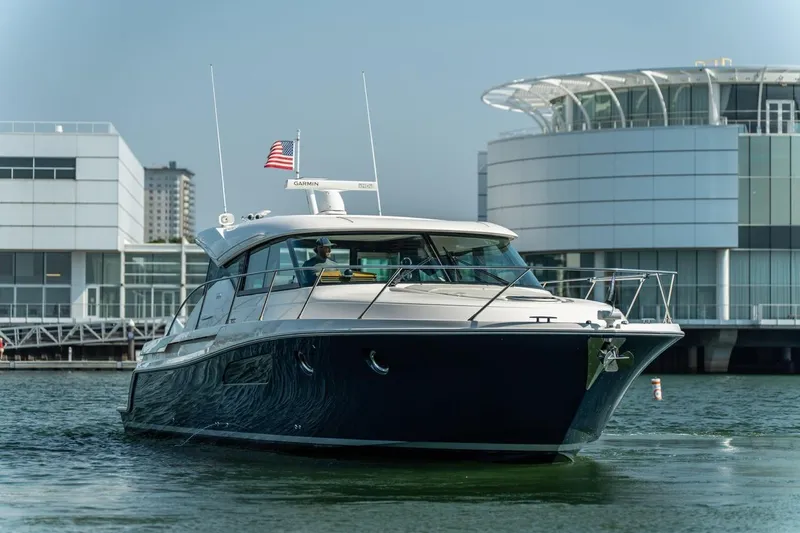 Escapade Yacht Photos Pics 2017 Tiara Yachts C44 Coupe cruising near modern waterfront buildings.