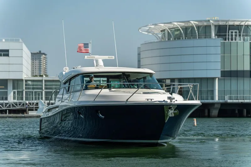 Escapade Yacht Photos Pics 2017 Tiara Yachts C44 Coupe cruising near modern waterfront buildings.