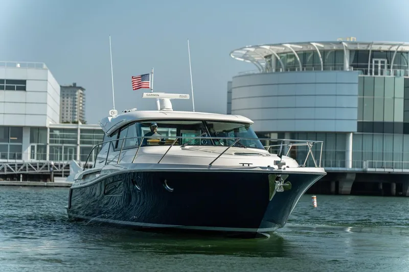 Escapade Yacht Photos Pics 2017 Tiara Yachts C44 Coupe cruising near modern waterfront buildings.