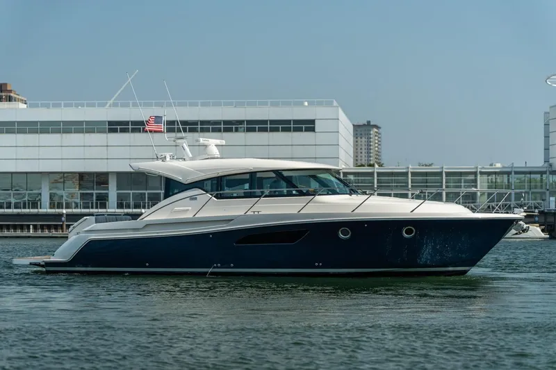 Escapade Yacht Photos Pics 2017 Tiara Yachts C44 Coupe in marina, sleek design, American flag, modern architecture backdrop.