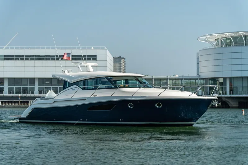 Escapade Yacht Photos Pics 2017 Tiara Yachts C44 Coupe cruising near modern waterfront buildings.