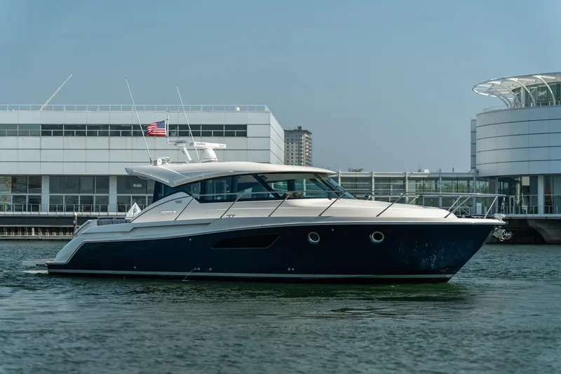Escapade Yacht Photos Pics 2017 Tiara Yachts C44 Coupe cruising near modern waterfront buildings.