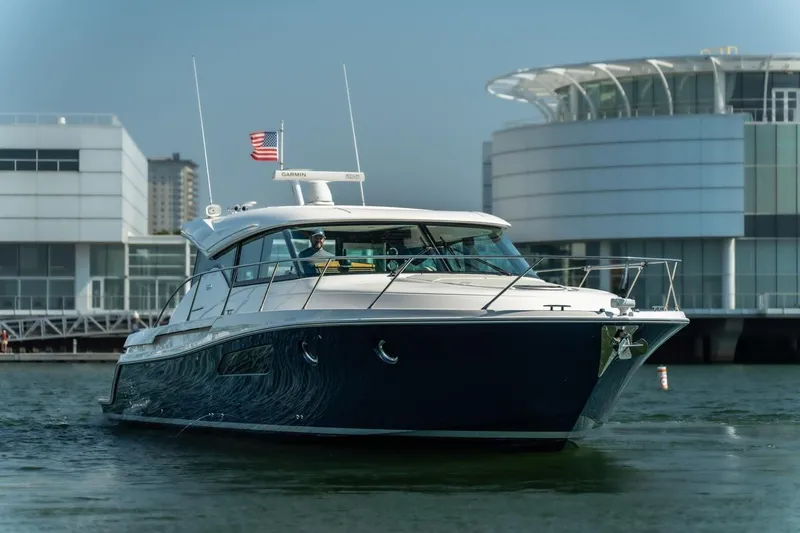 Escapade Yacht Photos Pics 2017 Tiara Yachts C44 Coupe cruising near modern waterfront buildings.