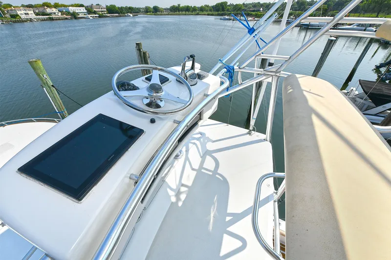  Yacht Photos Pics 1999 Cabo 45 Express boat helm with steering wheel and navigation screen, docked by a serene waterfront.