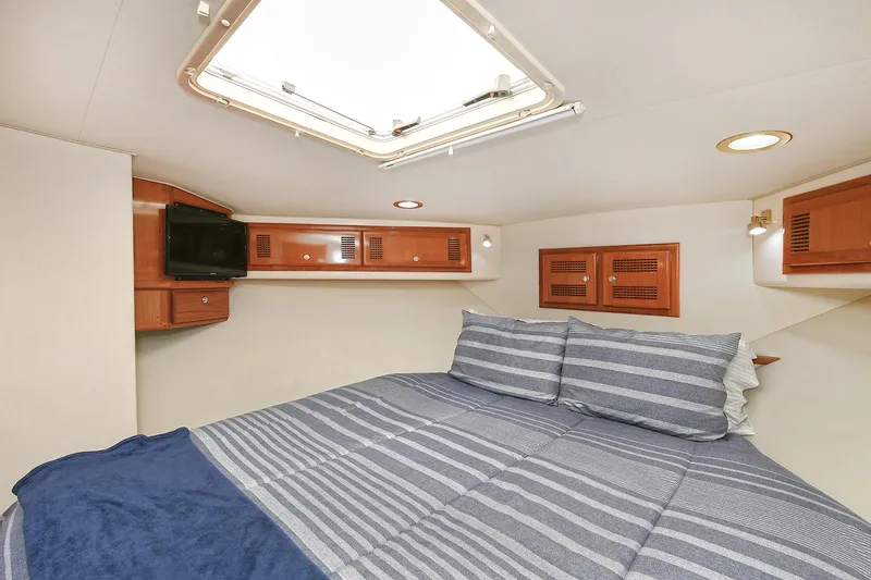  Yacht Photos Pics 1999 Cabo 45 Express cabin interior with bed, striped bedding, and wooden storage cabinets.