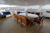 Spacious yacht deck with wooden dining table, chairs, and cushioned seating, 1966 Custom GLOBAL ENGINEERING.