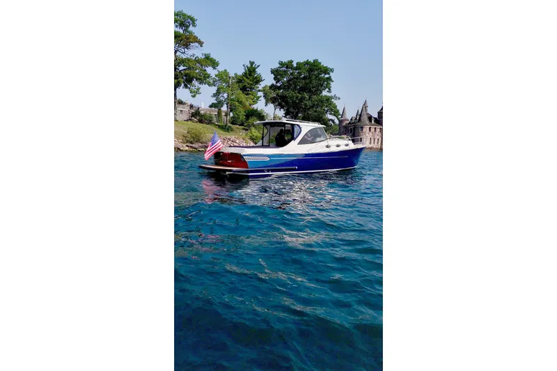  Yacht Photos Pics 2024 DaVinci 30HT boat on blue water, near shoreline with trees and buildings.