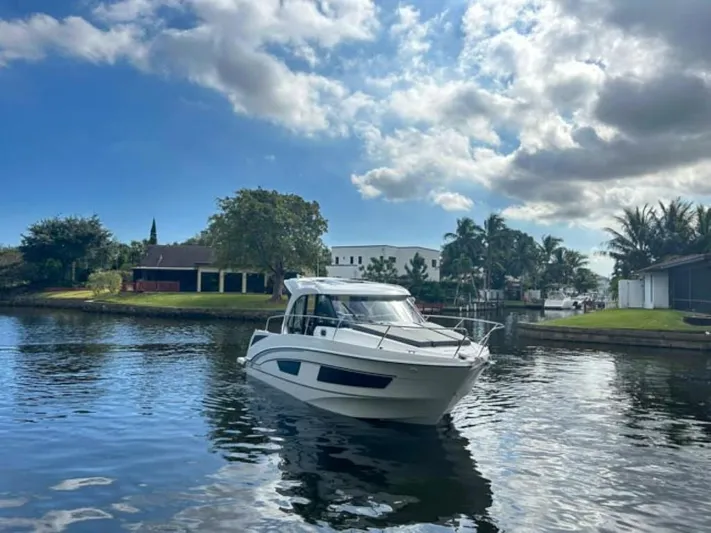  Yacht Photos Pics 2025 Beneteau Antares 9 boat cruising on a serene river under a partly cloudy sky.