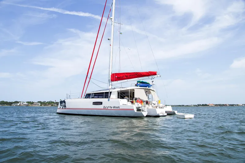 Out Of The Woods Yacht Photos Pics NEEL 51 Trimaran 2022 on calm water with red sail.