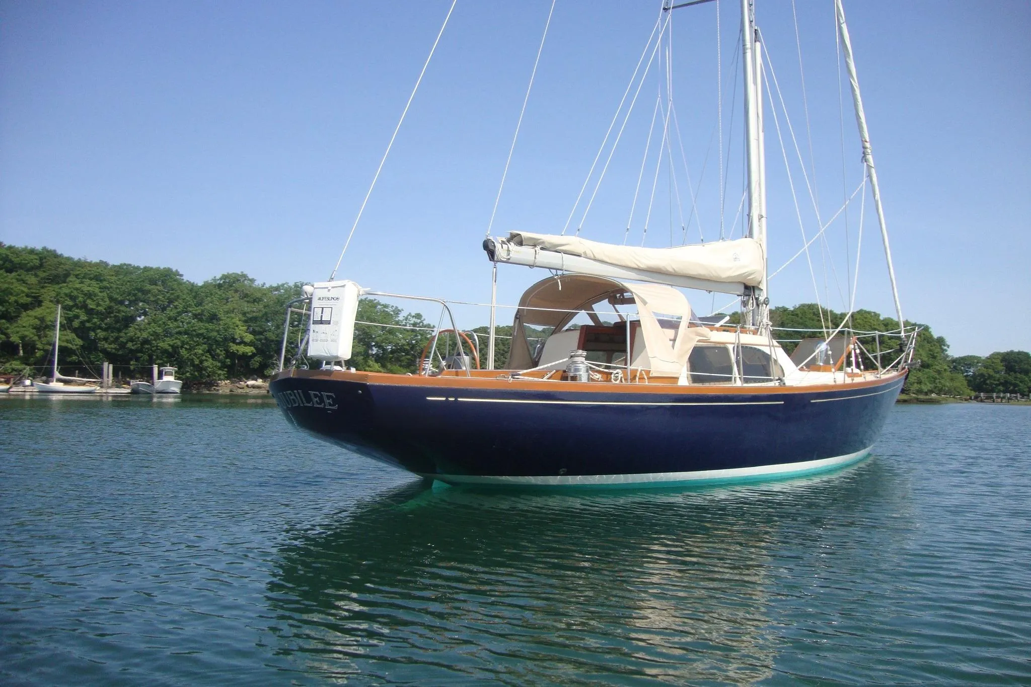 1967 Columbia Constellation sailboat on calm water, surrounded by lush greenery.