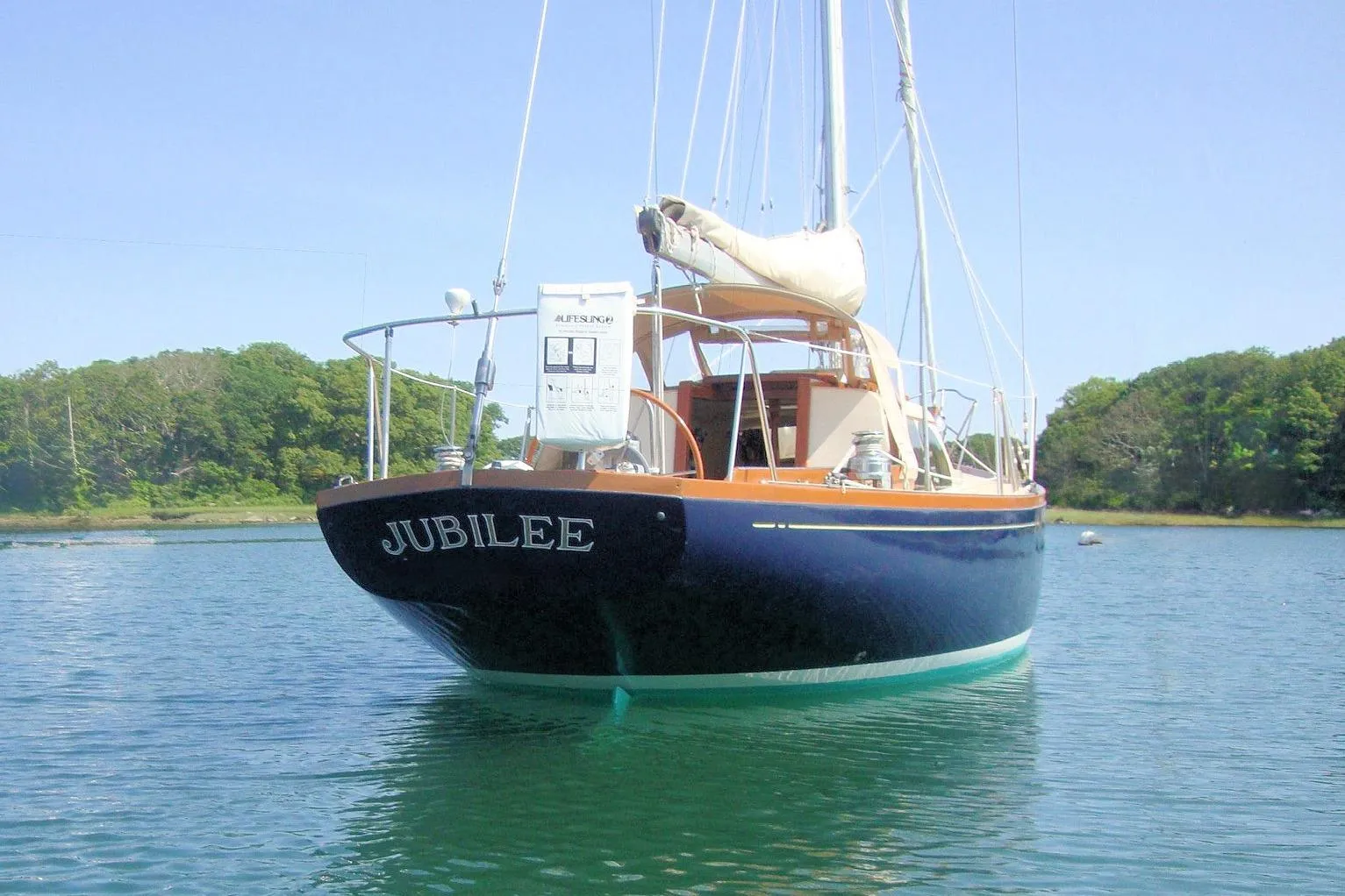 1967 Columbia Constellation sailboat "Jubilee" on calm water, surrounded by lush greenery.