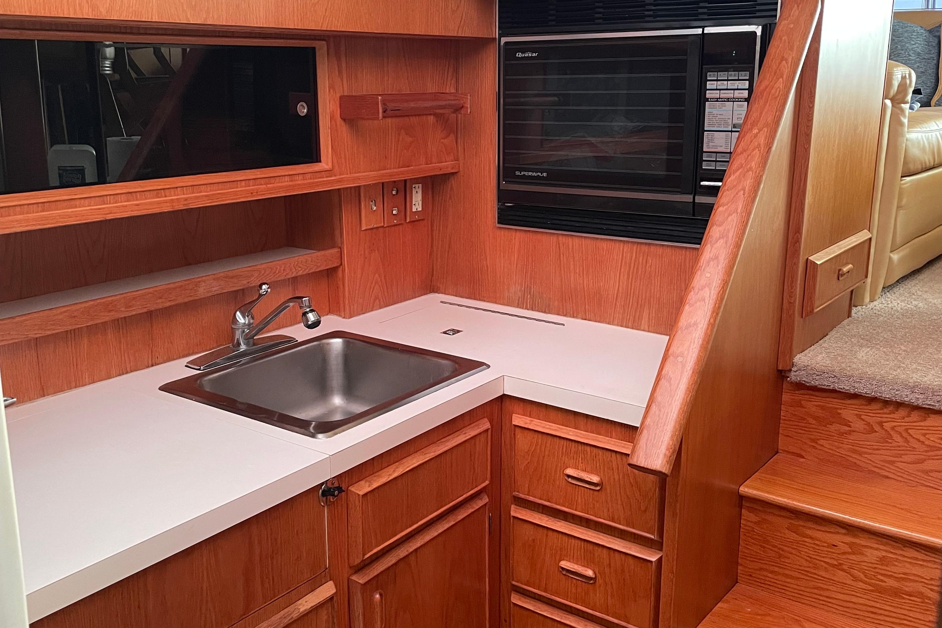1987 Bertram 42 Convertible yacht kitchen with sink, microwave, and wooden cabinetry.