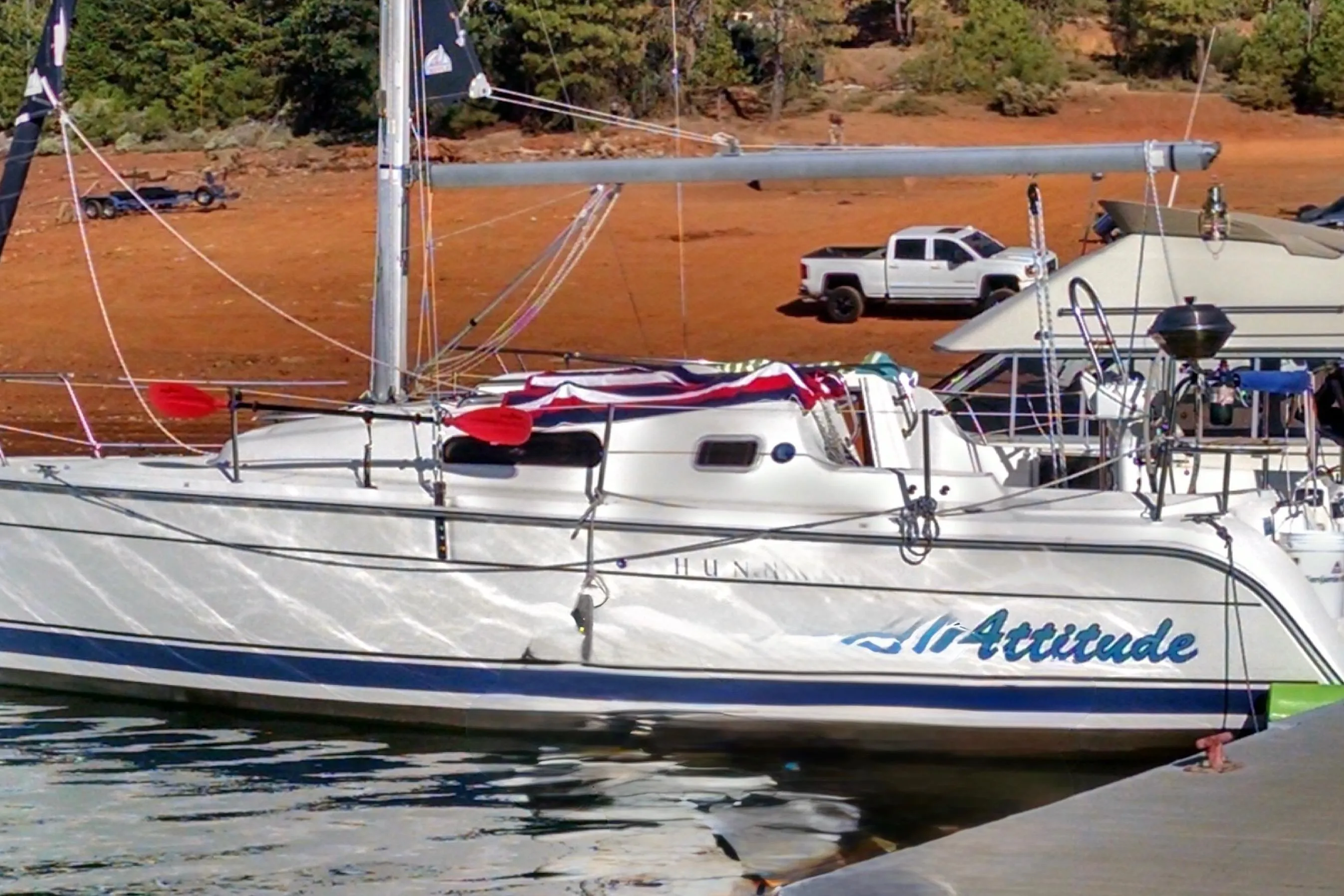 2008 Hunter 27 sailboat named "Attitude" docked by a lakeside with a truck nearby.