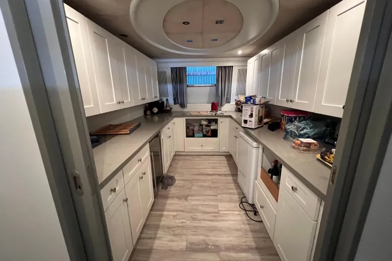 M/y Q Yacht Photos Pics Narrow kitchen with white cabinets, modern appliances, and wood flooring in a Falcon 106, 2001 model.