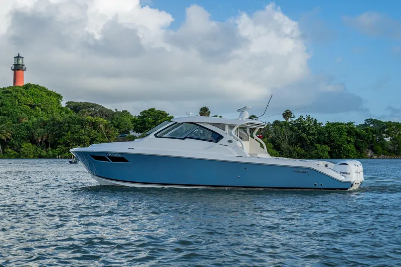  Yacht Photos Pics 2019 Pursuit DC 365 Dual Console boat on water near lush greenery and lighthouse.