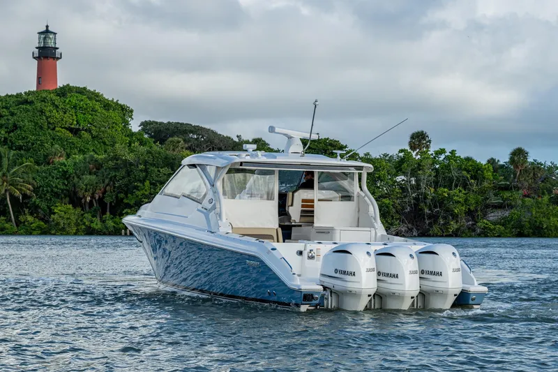  Yacht Photos Pics 2019 Pursuit DC 365 Dual Console boat on water near lush greenery and lighthouse.