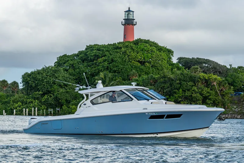  Yacht Photos Pics 2019 Pursuit DC 365 Dual Console boat cruising near lush greenery and lighthouse.