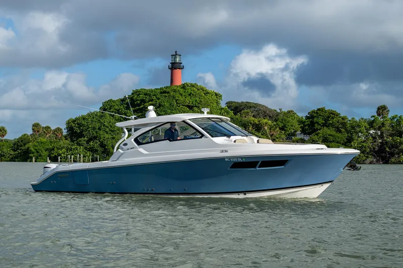  Yacht Photos Pics 2019 Pursuit DC 365 Dual Console boat cruising near a lighthouse and lush greenery.