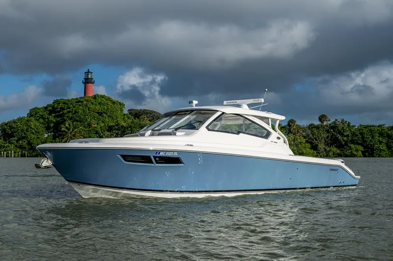 Yacht Photos Pics 2019 Pursuit DC 365 Dual Console boat on water near lush greenery and lighthouse.