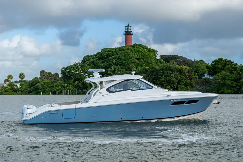  Yacht Photos Pics 2019 Pursuit DC 365 Dual Console boat cruising near lush greenery and lighthouse.