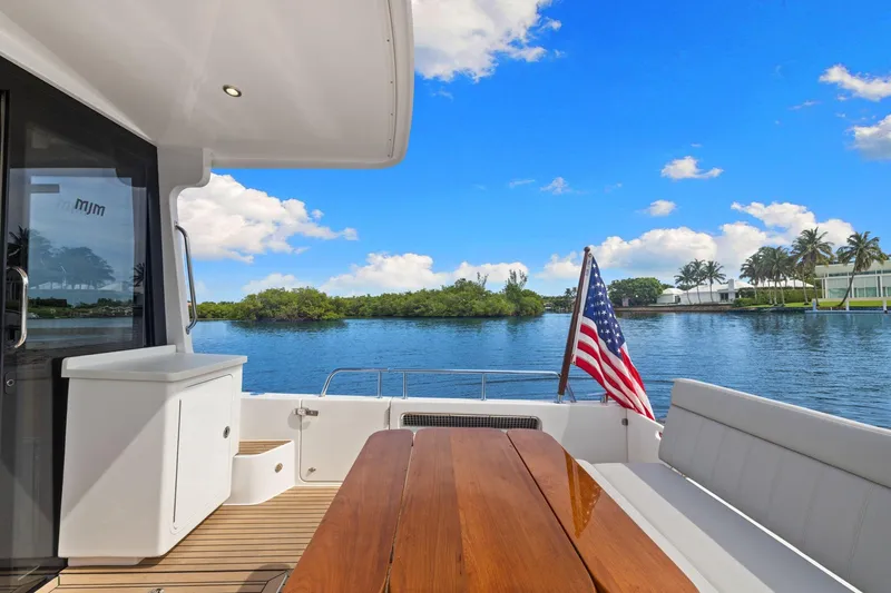 Mjm 42 For Sale Yacht Photos Pics 2024 MJM 42 yacht deck with American flag, wooden table, and scenic water view.