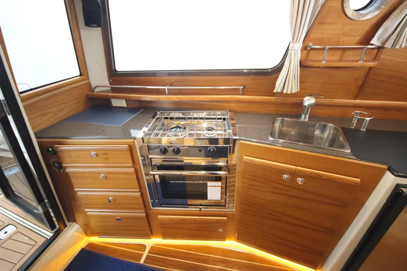 Patrick Mcginty Yacht Photos Pics 2022 Ranger Tugs R-29 Sedan Luxury Edition kitchen with stove, sink, and wooden cabinetry.