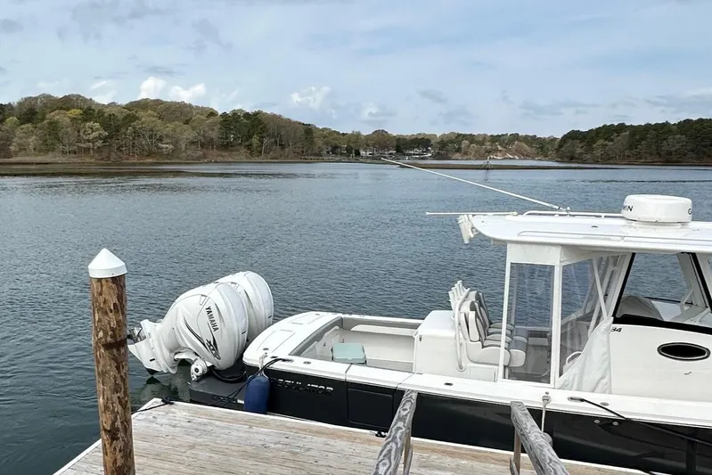 Grey Ghost Yacht Photos Pics 2023 Regulator 34 boat docked by a serene lake with wooded shoreline.
