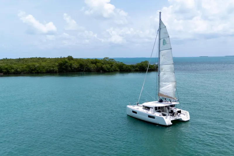 Wanderlust Yacht Photos Pics 2020 Lagoon 40 catamaran sailing in tranquil blue waters near lush green island.