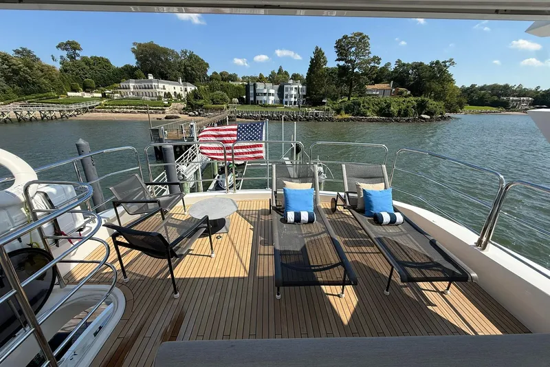  Yacht Photos Pics Sunseeker 76 Yacht 2021 deck with lounge chairs, American flag, and scenic waterfront view.